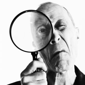 Monochrome portrait of senior man peering through magnifying glass, grimacing