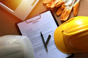 overhead image of a contract on a clipboard, construction helmet, gloves, edge of laptop