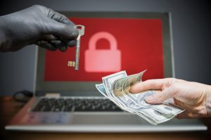 Hand representing hacker offering old-time key to another hand with cash, with a laptop in background with red screen and lock icon 